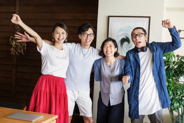 Group of young Japanese professionals in a co-working space, smiling and cheering at camera.