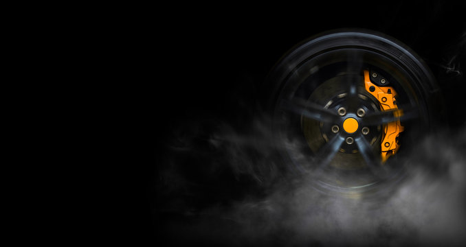 Isolated generic sport car wheel with yellow breaks drifting and smoking on a black background