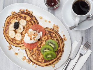 Pancakes with banana, kiwi, grapefruit and maple syrup on white marble table 