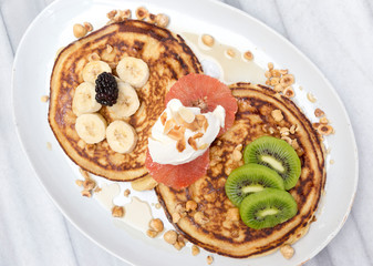 Pancakes with banana, kiwi, grapefruit and maple syrup on white marble table 