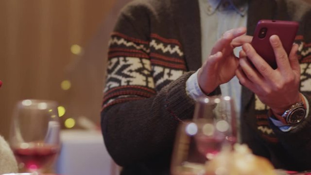 Row of multi-ethnic young people gathering at Christmas celebration table using smartphones for wireless internet communication. Modern online friendship. Nomophobia.
