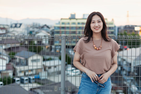 Young Japanese woman standing on a rooftop in an urban setting, looking at camera.