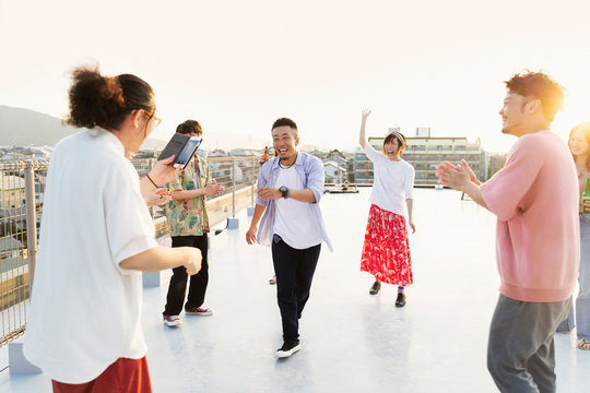 Group of young Japanese men and women dancing on a rooftop in an urban setting.