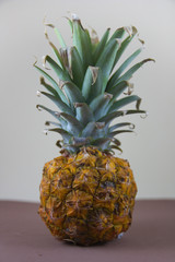 Small pineapple with green leaves on a neutral table