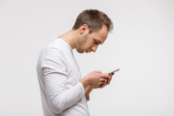 Close up portrait of man looking and using smart phone with scoliosis, side view, isolated on gray...