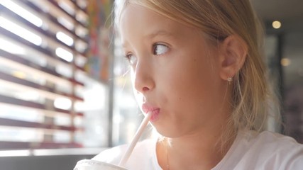 Little girl child in cafe drinking milk cocktail cacao with milk. Child drinks a milkshake sits in a cafe.