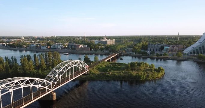 Train riding on a scenic railroad bridge over a river with city Riga in background. Aerial view, 4K drone video. 