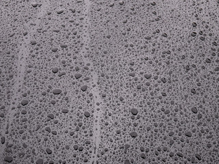 Hood of a metallic black vehicle full of drops of water of different sizes on a rainy day