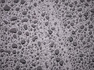 Hood of a metallic black vehicle full of drops of water of different sizes on a rainy day