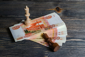 two chess pieces stand on wads of Russian money, the black king fell before the white chess king