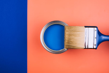 Brush on open can of blue paint on coral and blue background. Concept of changing color of the year.