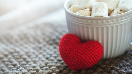 Background with gray cup with marshmallows and red heart on knitted napkin. warm drink with grey scarf.