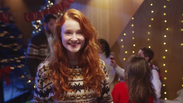 Beautiful esctatic girl with cute ginger hair and smile staying at Christmas winter party celebrating New Year's Eve holidays in circle of best friends.
