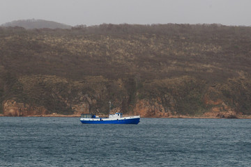 Blue pleasure tourist boat goes on the water against the backdrop of the autumn hills of Reinike Island near Vladivostok