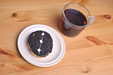 A donut with peanut as a topping and a cup of coffee on top of wooden table.
