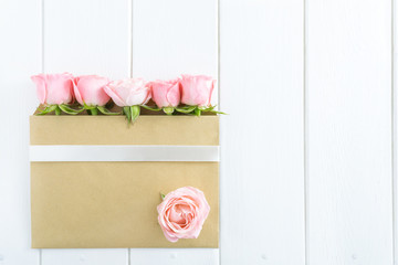 Pink roses in envelope with white ribbon on white wooden background. Flat lay, top view, copy space.