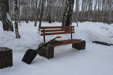 snow shovel and broom for cleaning on an empty street bench in the Park in winter