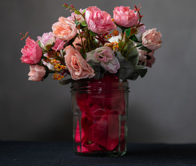 Glass jar with red rose petals and a bouquet of colorful flowers.