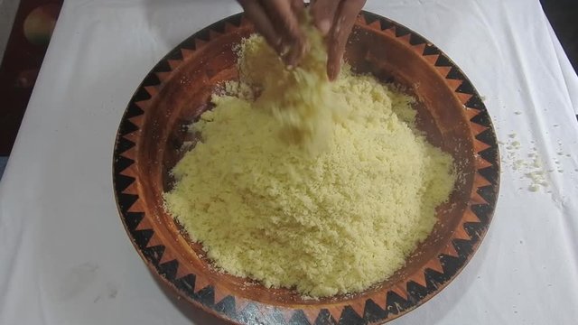 Woman rolling hot semolina of couscous between  her fingers in a wooden dish at home  after steaming it .Close Up 
of plate Couscous. Top view .Morocco