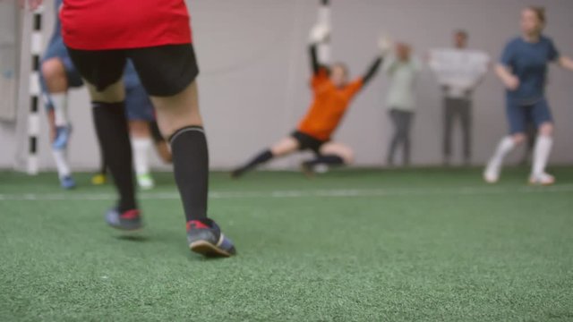 Low section selective focus shot of female soccer player shooting free kick, scoring a goal and celebrating victory with team during game on indoor sports field