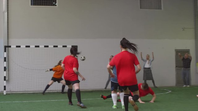 Female soccer player dribbling ball and shooting it but missing goal during match on indoor sports field