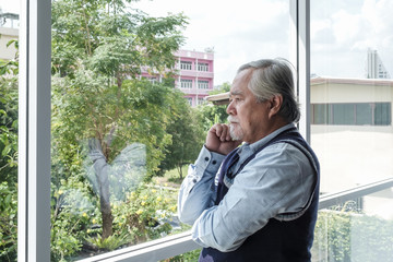 Portrait of elderly Asian senior man with grey hair looking out window for thinking business...