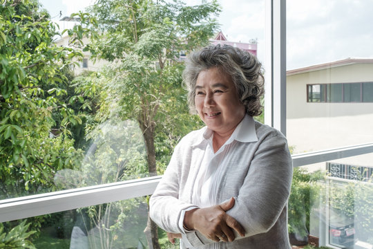 Portrait of elderly Asian woman with grey hair smiling and happy standing near window, lifestyle concept
