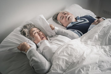 elderly couple caucasian senior woman and man sleep on bed and snoring in white blanket in bedroom,...