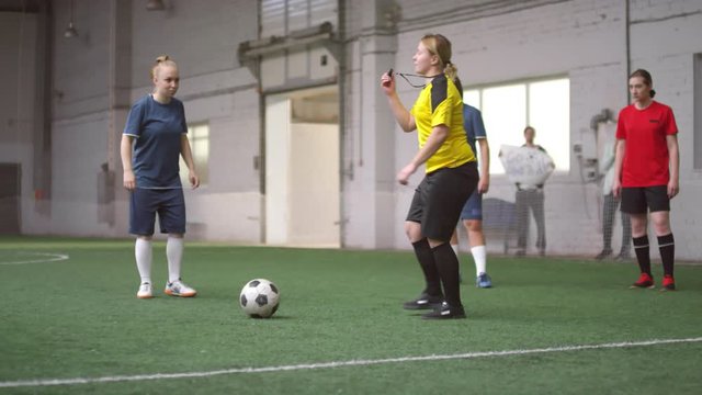 Soccer referee placing ball on sports field in front of female player for taking penalty kick during match on indoor sports field