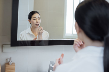 Asian woman wearing white shirt and make up face in front of mirror in bathroom
