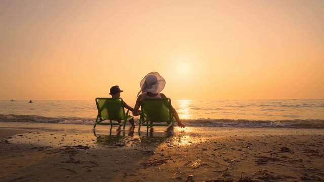 Mother and son wiith hats playing on the beach at the sunset time sitting on chairs. Concept of friendly family