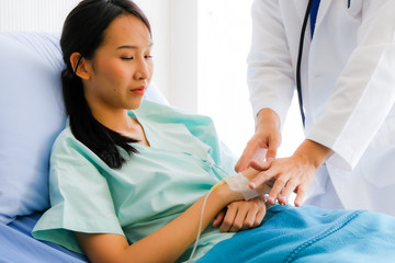 Young male doctor holding Asian female patient hand at hospital bed and hand with fluid replacement therapy, saline intravenous for set,Healthcare and medically concept