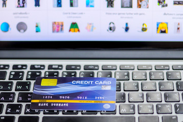 Blue credit card mockup put on keyboard of laptop and blurred web shopping online on display monitor, online shopping and payment via credit card concept