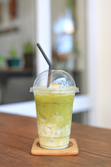 Iced matcha green tea latte with milk with brown straw in take away cup on wooden table at cafe.