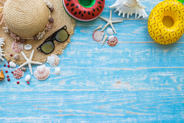 Travel concept with inflatable fruit shape coaster straw hat sunglasses and seashell on blue color wood background.