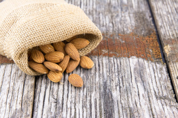 Raw almonds spilling burlap sack old wood table .