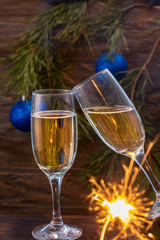 Glasses of champagne with bubbles on the background of Christmas decorations. Glasses touch during a festive toast and sparklers burn beautifully. Beautiful card.
