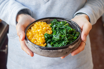 Bulgur cereal cooked. In bowl with vegetables. Vegan, vegetarian food. Woman holds in hands on legs a bowl with bulgur pilaf.
