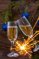 Glasses of champagne with bubbles on the background of Christmas decorations. Glasses touch during a festive toast and sparklers burn beautifully. Beautiful card.