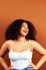 pretty young african american woman with curly hair posing cheerful gesturing on brown background, lifestyle people concept