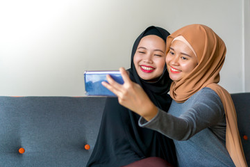 Two Malay friends wearing hijab at the sofa