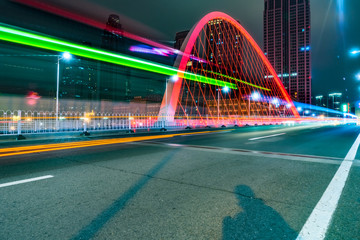 car light trails on steel bridge with city skyline.