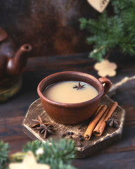 Spicy masala tea in a clay terracotta cup on a wooden board against a dark brown background with a...