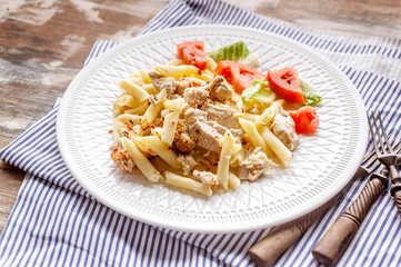 Close-up pasta Penne with chicken, smoked cheese and spices on a white plate. Traditional Mediterranean Italian cuisine.