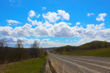 A beautiful spring day after rain in the countryside. The blue sky in the clouds and the road that goes into the distance. Early spring. The first leaves on the trees, green grass breaks through.