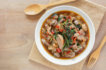 top view of stir fried duck meat with holy basil in a ceramic dish on wooden table. hot and spicy thai style food menu.