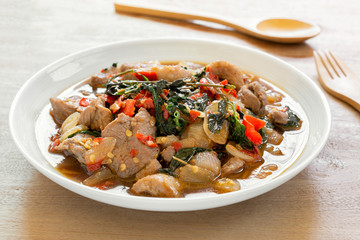 close up of stir fried duck meat with holy basil in a ceramic dish on wooden table. hot and spicy...