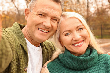Happy mature couple taking selfie in autumn park