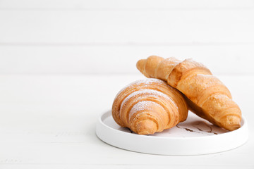 Plate with tasty croissants on white table