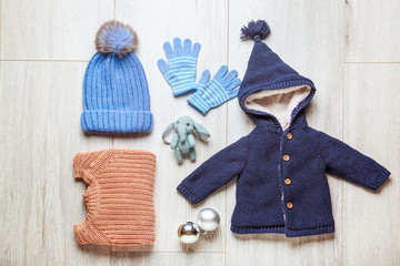 Set of kid winter clothes with toy and Christmas balls on wooden background